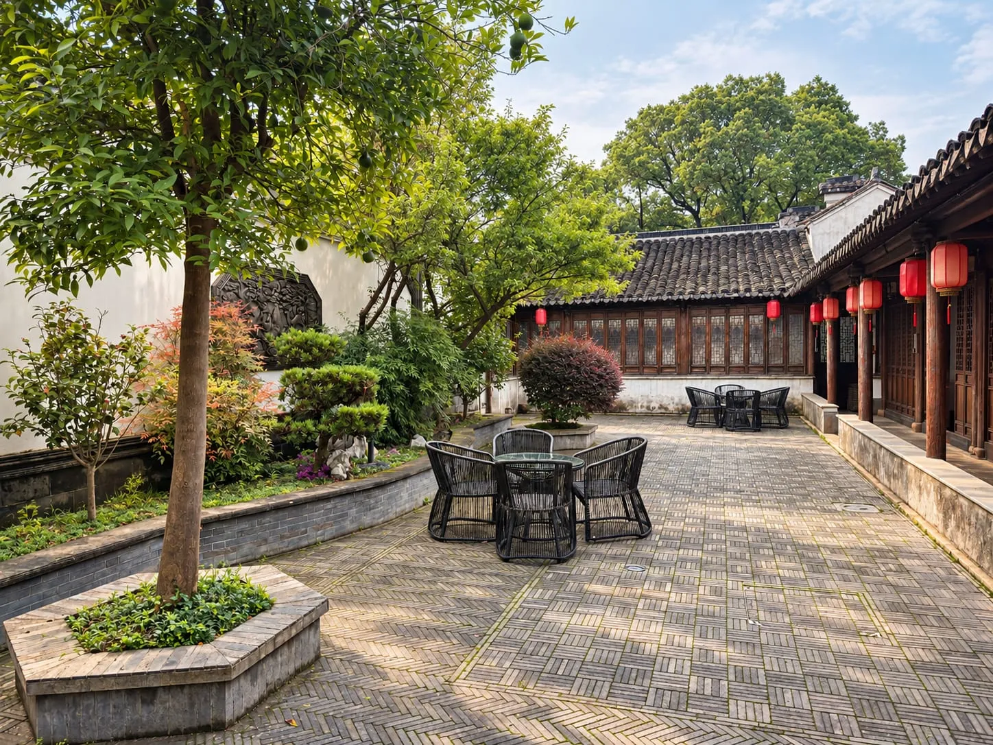 A paved garden courtyard with outdoor tables, beside a wooden veranda hung with red lanterns